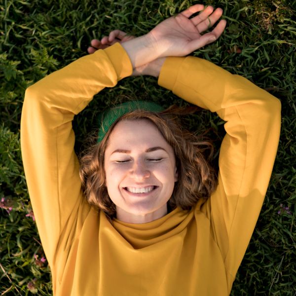 smiling lady wearing yellow top and a green hat lying on grass
