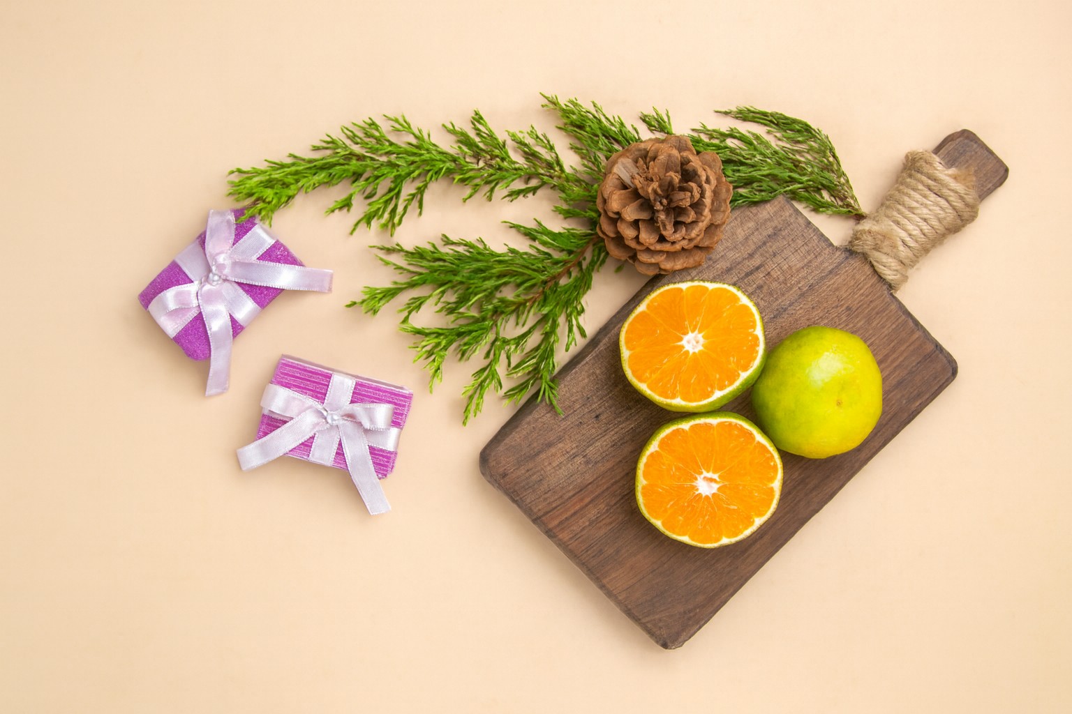 A wooden chopping board with citrus fruit on it and a pine cone next to it. Two small wrapped gifts at the side. By KamranAydinov at Freepik