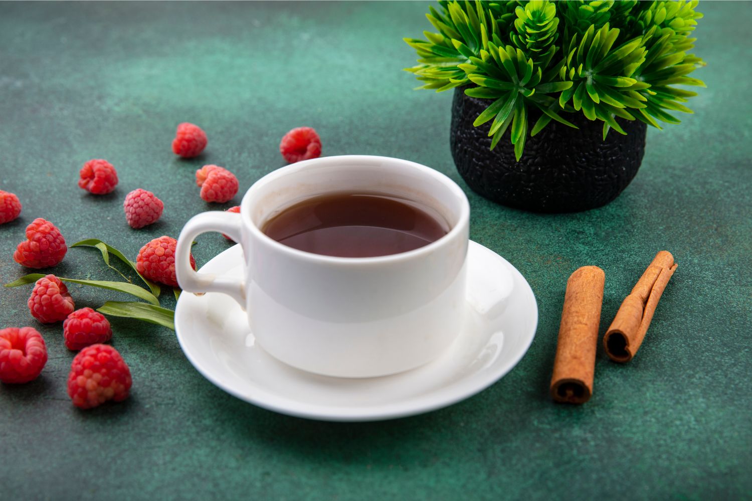 White cup and sauce containing black coffee with raspberries and cinnamon scattered next to it